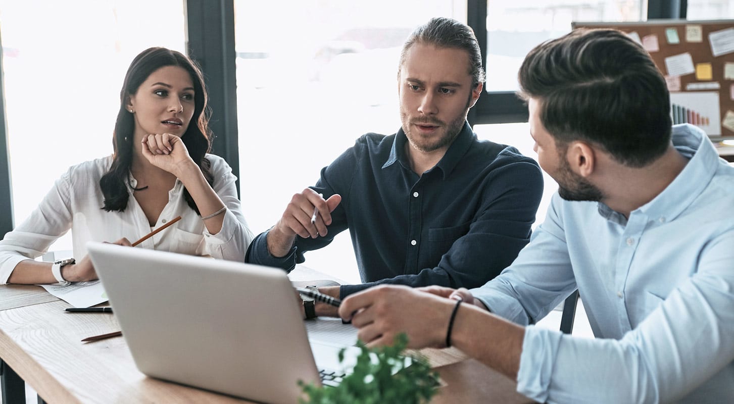 Three people seated at a table, collaborating over a laptop during a meeting.